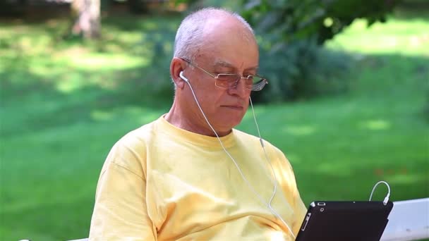 Старший чоловік насолоджується музикою на своєму цифровому планшетному ПК — стокове відео