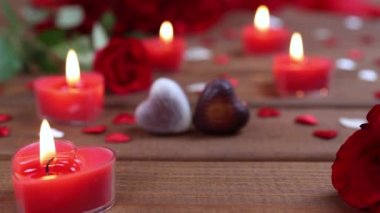 Sevgililer Günü konsepti çikolatalı şekerler kalp şeklinde ve ahşap üzerinde mumlar olan kırmızı güller. Aşk ve aşk kavramı. Dolly 4K çekti.