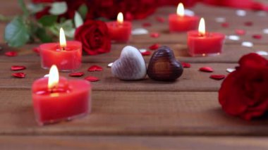 Sevgililer Günü konsepti çikolatalı şekerler kalp şeklinde ve ahşap üzerinde mumlar olan kırmızı güller. Aşk ve aşk kavramı. Dolly 4K çekti.