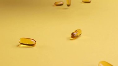 Omega balığı yağı besin takviyesi sarı arka plana düşüyor. Omega balığı yağı softgels beslenme takviyesi arka planı. Sağlıklı yaşam ve kalp sağlığı kavramı. Yavaş çekim