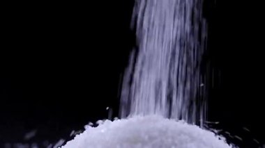 Ağır çekimde siyah arkaplana beyaz şeker dökülüyor. Sağlık kavramına yönelik şeker tüketiminin faydaları veya tehlikesi.