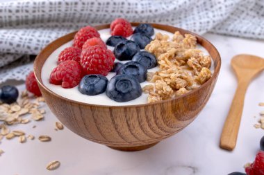Bir porsiyon yoğurt, yabanmersinli ahududu ve ahşap bir kasede servis edilmeye hazır yulaf gevreği. Diyet konsepti için sağlıklı yiyecekler. Yoğurtlu meyveli müsli..