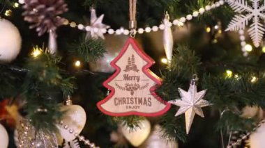 Noel ağacında asılı Mutlu Noeller mesajı olan ahşap Noel süslemesi. Noel 'i dekorasyon ve ışık konseptiyle kutluyoruz. Dolly 4K çekti.