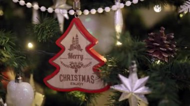 Noel ağacında asılı Mutlu Noeller mesajı olan ahşap Noel süslemesi. Noel 'i dekorasyon ve ışık konseptiyle kutluyoruz. Dolly 4K çekti.