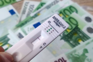 Corna virüsü kendi kendini test etti ve covid-19 virüsü için hızlı bir antijen testi yaptı. Birkaç avroluk banknotlarla dolu bir kaset. Para kazanma kavramı