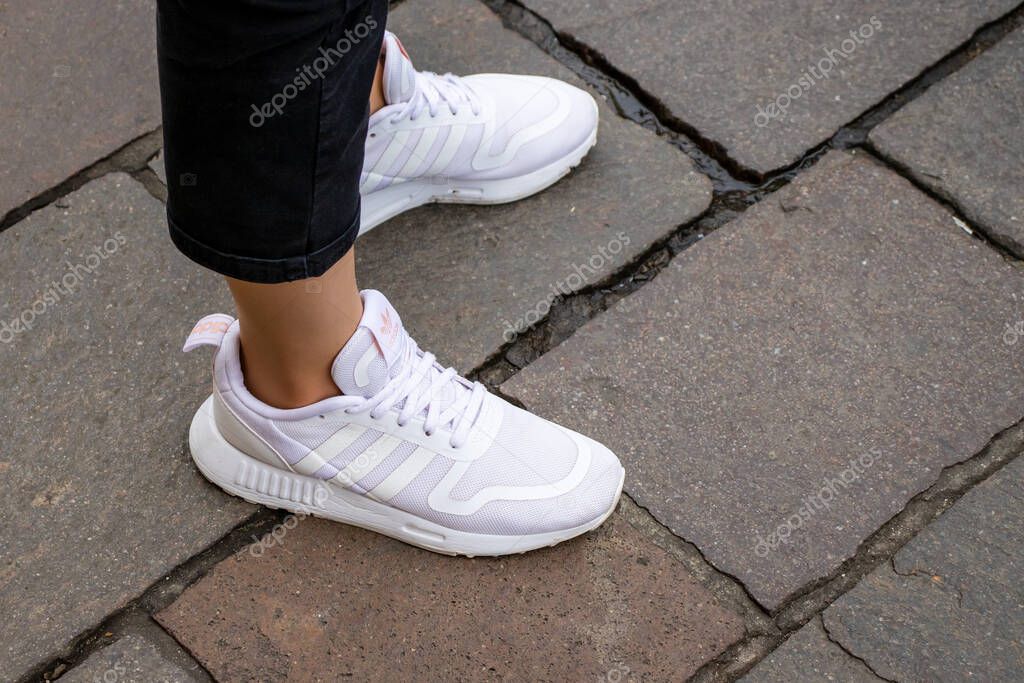 Warsaw Poland, October 2, 2022: Feet wearing white Adidas shoes. girl legs wearing white color sneakers.  Women wearing Adidas white shoes