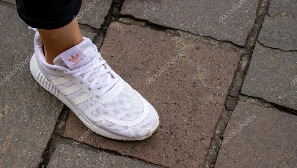 Warsaw Poland, October 2, 2022: Feet wearing white Adidas shoes. girl legs wearing white color sneakers.  Women wearing Adidas white shoes