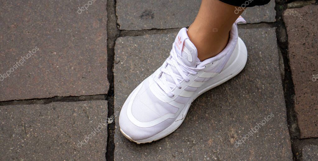 Warsaw Poland, October 2, 2022: Feet wearing white Adidas shoes. girl legs wearing white color sneakers.  Women wearing Adidas white shoes