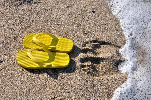 Yellow flip flops on the beach sand — Stock Photo, Image