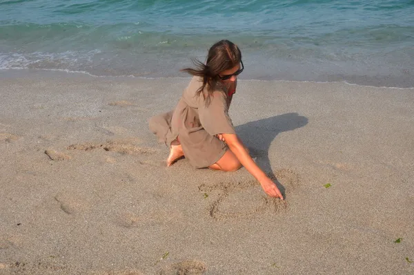 Girl draws a heart in the sand
