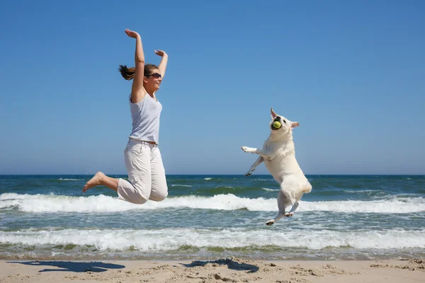 Mujer y raza de perro Labrador saltando en la playa —  Fotos de Stock