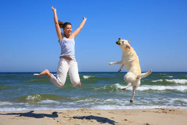 Mulher e cão raça Labrador saltando na praia — Fotografia de Stock