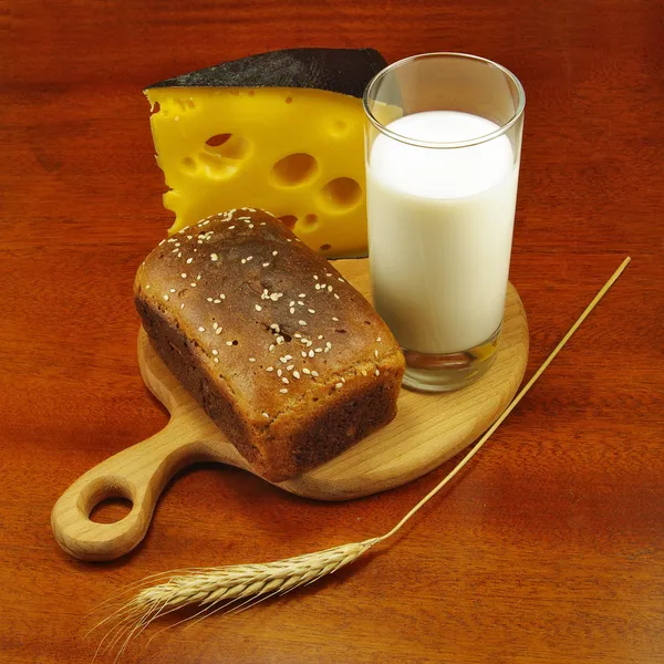 image of a glass of milk, bread on the board, wheat and cheese closeup