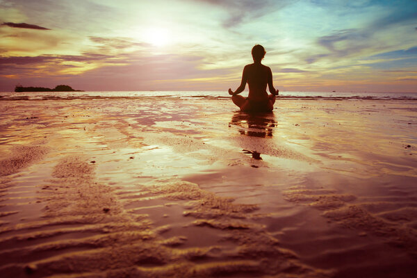 силуэт женщины медитирующей на пляже
