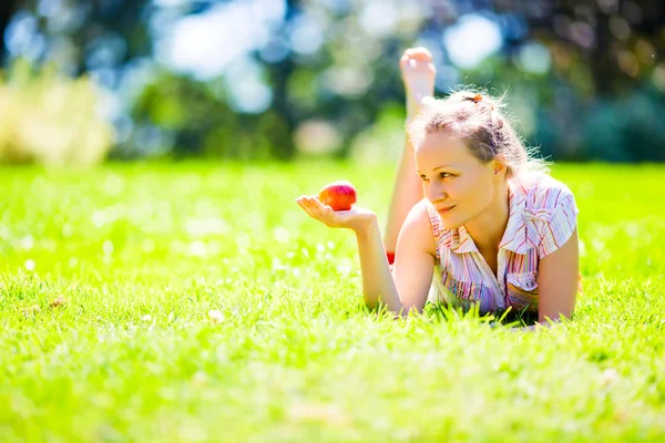 Girl on green grass looking on red apple — Stock Photo, Image