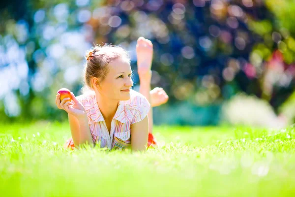 Girl with an apple on green grass — Stock Photo, Image