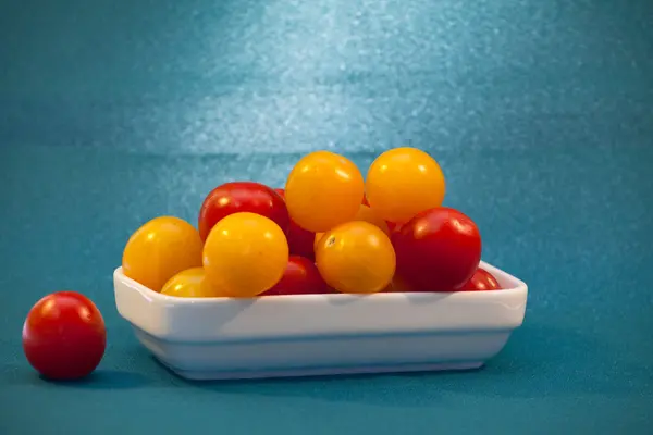 Tomates cherry rojos y amarillos en un plato blanco sobre un fondo azul —  Fotos de Stock