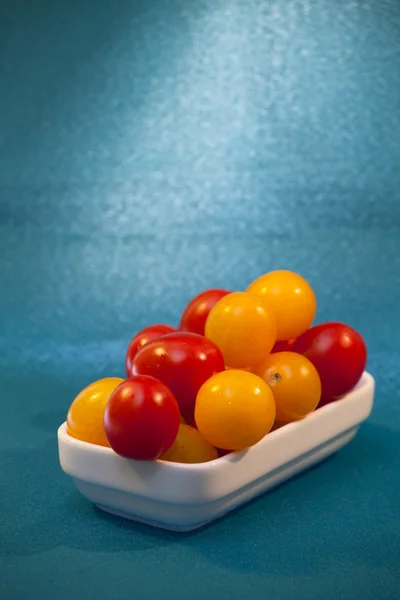 Red and yellow cherry tomatoes in a white plate on a blue backgr — Stock Photo, Image