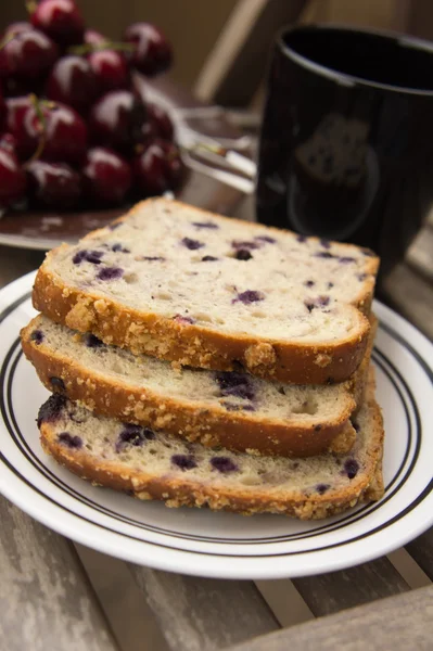 Blueberry bread with red cherries and tea on a wooden table — Stock Photo, Image