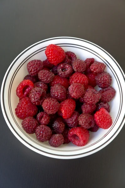 A bowl of raspberries on a black wooden table closeup — Zdjęcie stockowe