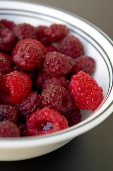 A bowl of raspberries on a black wooden table closeup — Stock Photo, Image