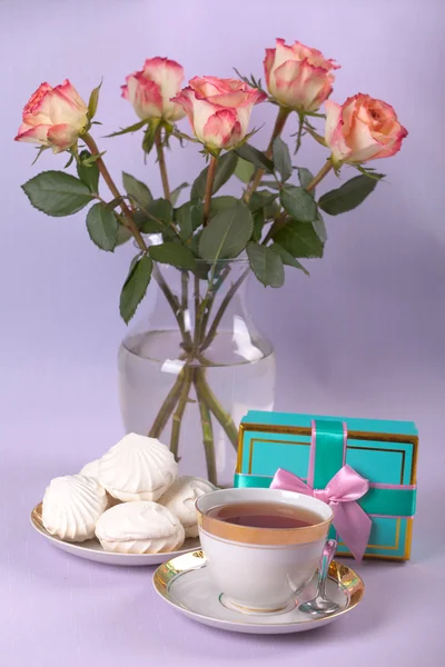 A cup of tea with white souffle and roses in vase and present — Stock Photo, Image