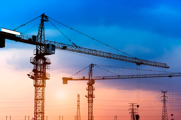 Grúas de construcción industrial y siluetas de construcción sobre el sol al amanecer. — Foto de Stock