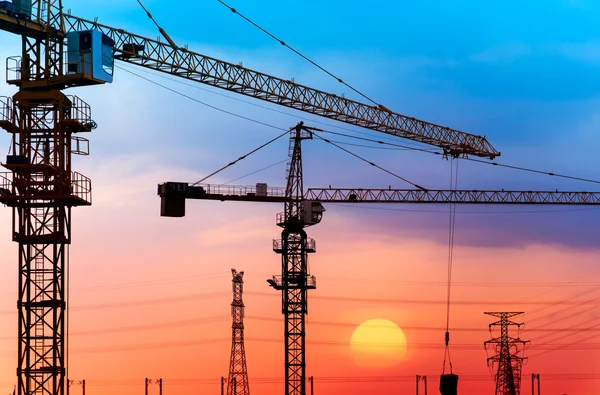 Gru industriali da costruzione e sagome di edifici al sole all'alba. — Foto Stock