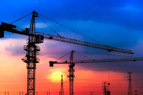 Industriële bouwkranen en silhouetten boven de zon bij zonsopgang. — Stockfoto