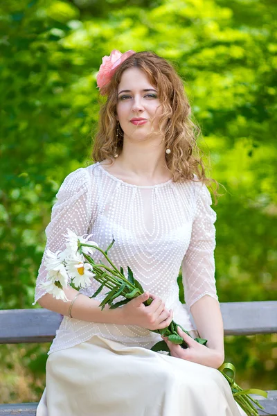 Eine schöne junge Frau mit lockigem Haar und Gänseblümchen in der Hand — Stockfoto