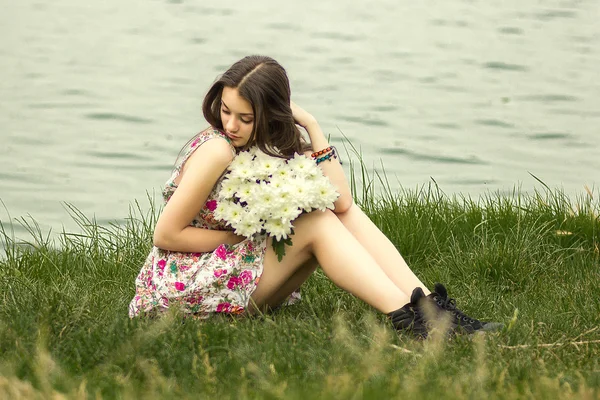 Beautiful young brunette woman sitting on the grass with a bouquet of flowers — Stock Photo, Image