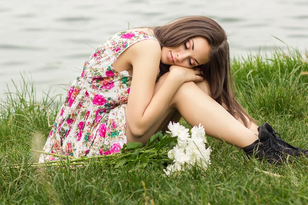 Schöne junge brünette Frau sitzt auf dem Gras mit einem Blumenstrauß — Stockfoto