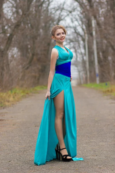 Retrato de bela jovem mulher de cabelos castanhos com cabelo bonito e maquiagem profissional em um vestido azul longo com fenda alta — Fotografia de Stock