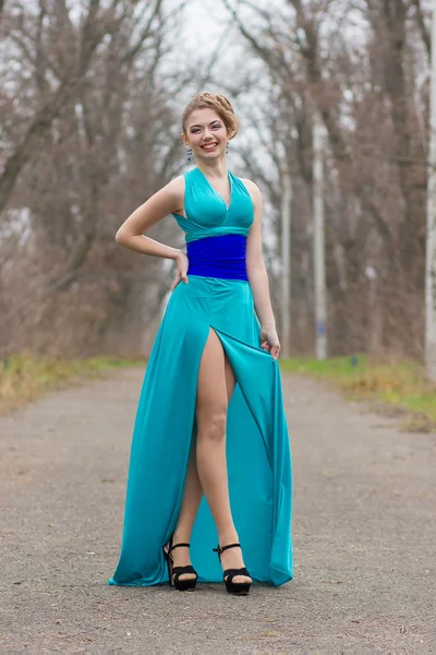 Porträtt av vacker ung brunhårig kvinna med vackra hår och makeup professionell i en lång blå klänning med hög slit — Stockfoto