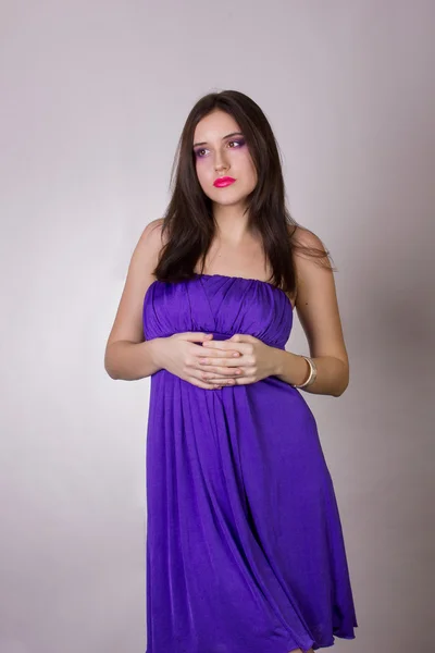 Emocional retrato de estudio de una hermosa chica morena en un vestido de cóctel y maquillaje de noche brillante lila con labios rosados — Foto de Stock