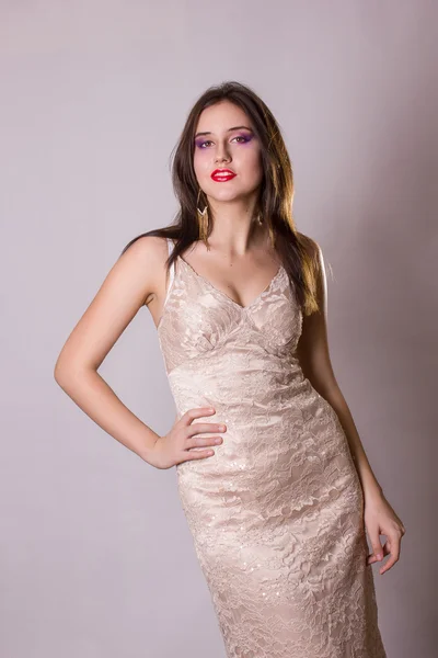 Studio portrait of a beautiful and sexy young brunette woman in evening beige lace dress and long gold earrings — Stock Photo, Image