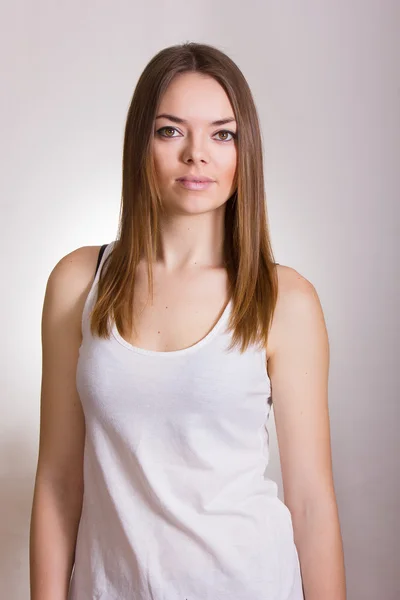 Retrato de uma bela jovem mulher em uma camiseta branca com maquiagem natural e cabelo castanho liso — Fotografia de Stock