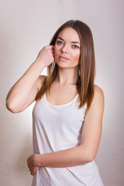 Портрет красивой молодой женщины в белой футболке с натуральным макияжем и прямыми каштановыми волосами
