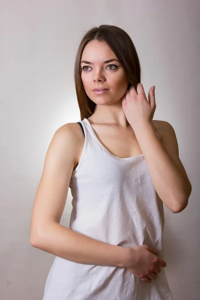 Retrato de uma bela jovem mulher em uma camiseta branca com maquiagem natural e cabelo castanho liso — Fotografia de Stock