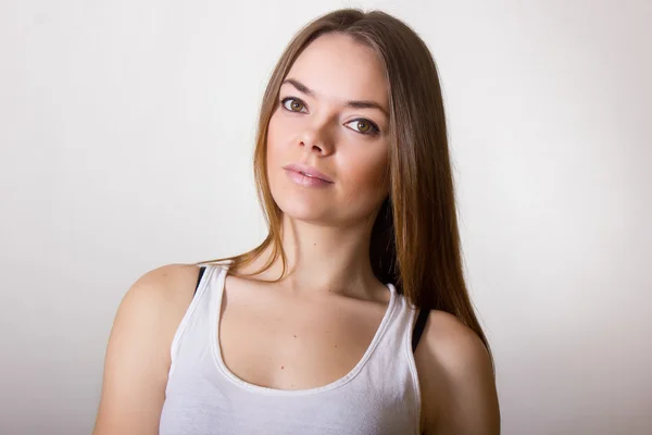 Retrato de uma bela jovem mulher em uma camiseta branca com maquiagem natural e cabelo castanho liso — Fotografia de Stock