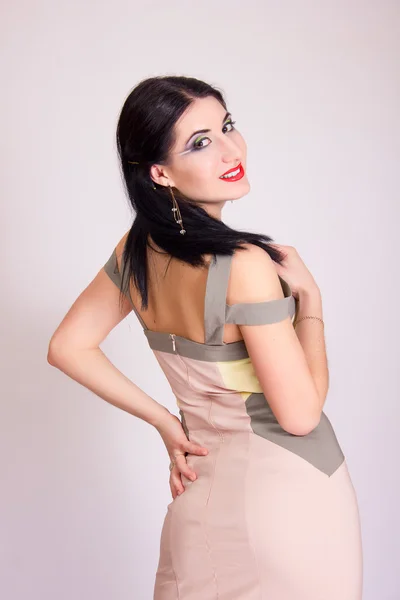 Portrait of beautiful young brunette woman in studio with bright evening make-up in a short beige dress — Stock Photo, Image