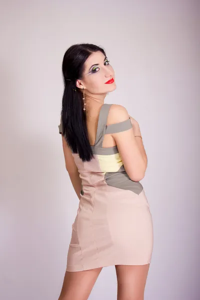 Portrait of beautiful young brunette woman in studio with bright evening make-up in a short beige dress — Stock Photo, Image