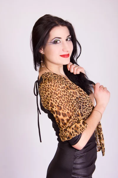 Studio portrait of a beautiful slim brunette girl in a short tight black dress with leopard bolero — Stock Photo, Image