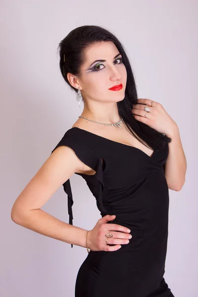 Beautiful slim young brunette woman in evening black dress and jewelry — Stock Photo, Image