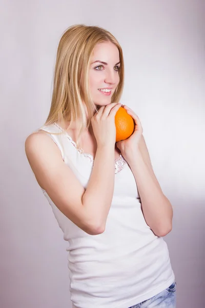 Belle jeune fille blonde posant sur un fond blanc dans le studio avec une orange dans les mains — Photo