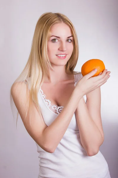 Menina loira bonita posando em um fundo branco no estúdio com uma laranja nas mãos — Fotografia de Stock