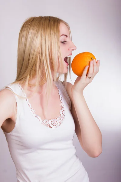 Schöne junge blonde Mädchen posiert auf weißem Hintergrund im Studio mit einer Orange in den Händen — Stockfoto