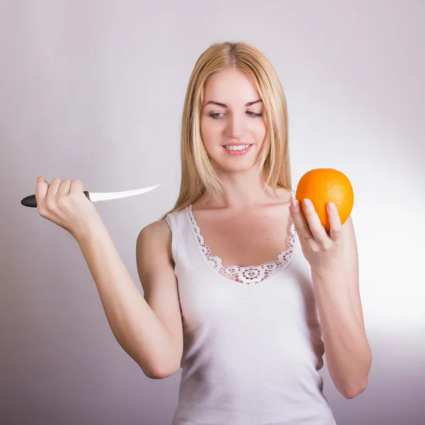Schöne junge blonde Mädchen posiert auf weißem Hintergrund im Studio mit einer Orange in den Händen — Stockfoto