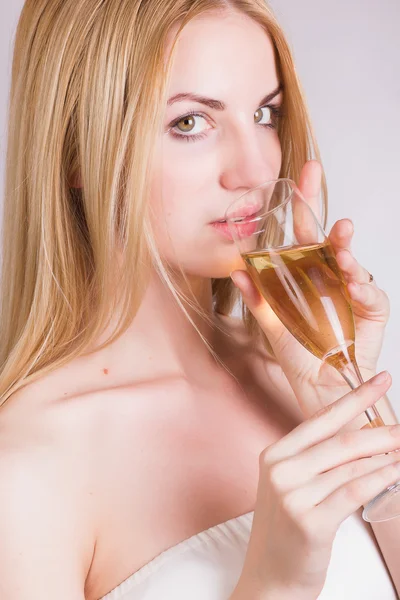 Portrait of a beautiful young blonde woman on a white background in a short white dress with black lace. Cute girl posing with a glass of champagne in her hands. — Stock Photo, Image