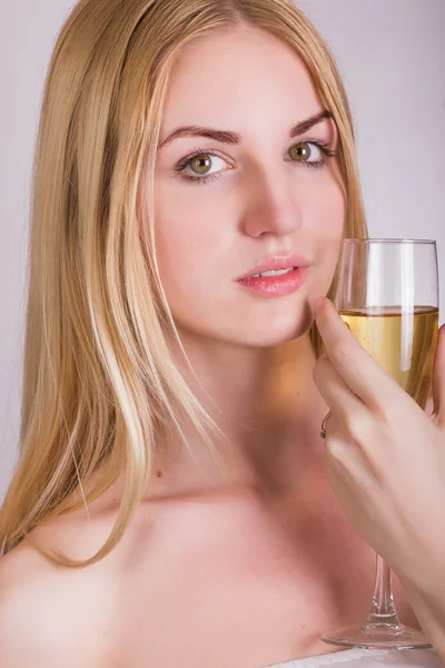 Portrait of a beautiful young blonde woman on a white background in a short white dress with black lace. Cute girl posing with a glass of champagne in her hands. — Stock Photo, Image